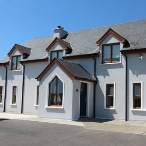 Exterior view of a house with light grey walls, crisp white decorative trim, and warm brown window frames.